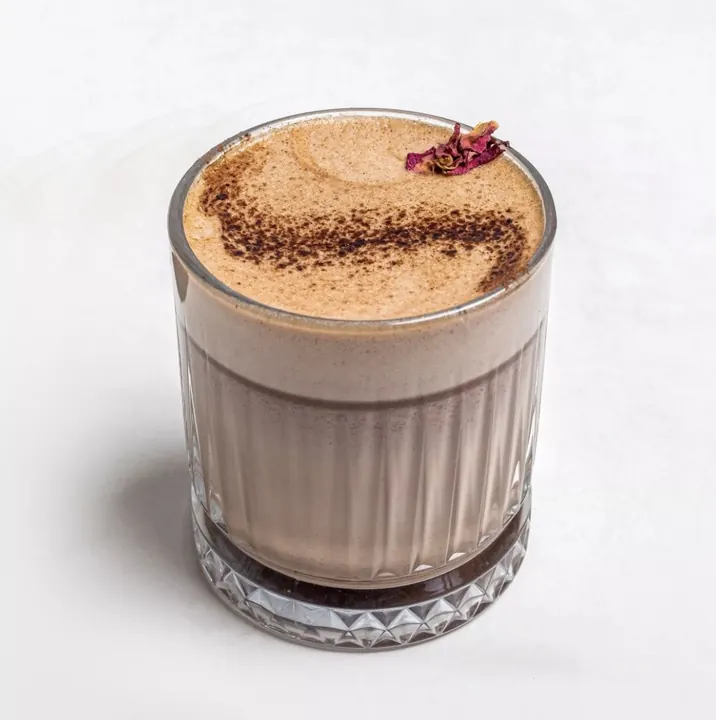Cacao milk drink with a frothy dusted top in a ribbed glass