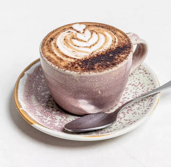 Coffee with latte art served in a speckled stoneware cup and saucer