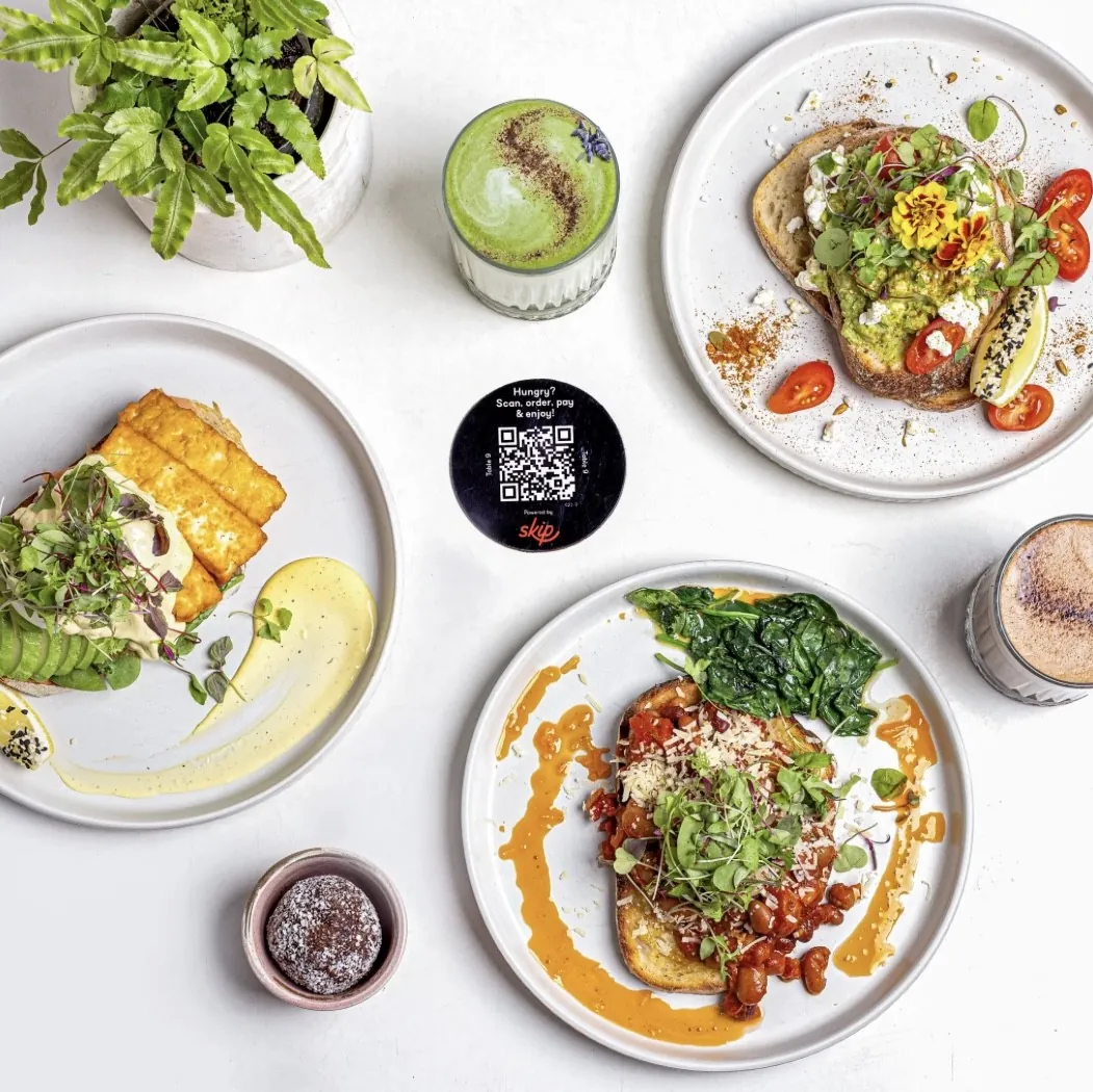 Overhead table spread with spiced beans on sourdough, salad bowls, coffee and a bliss ball