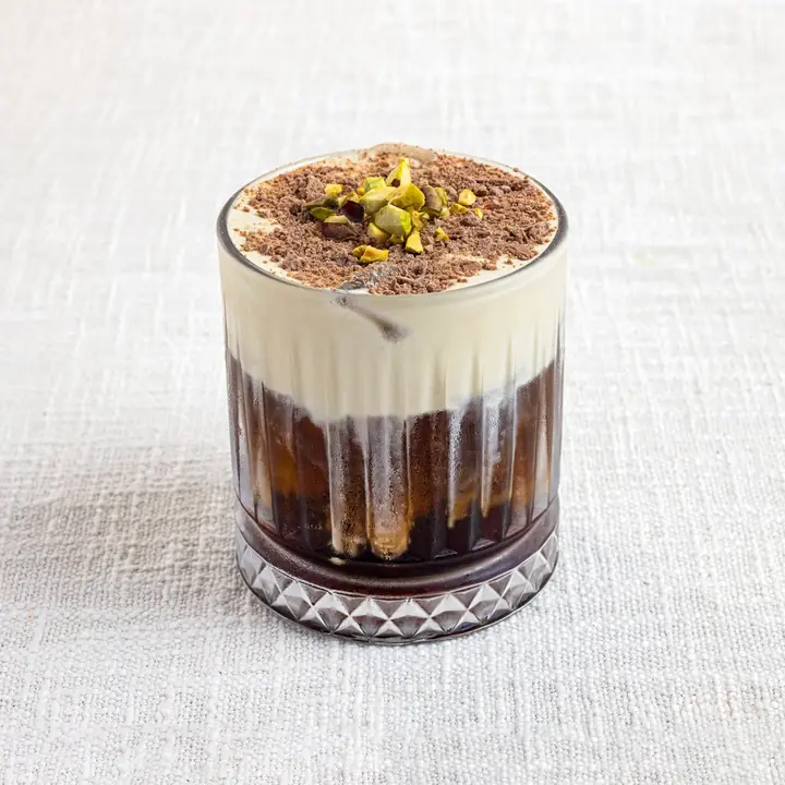 Pistachio cold brew topped with cream in a ribbed glass