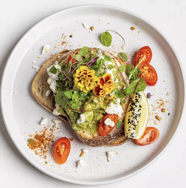 Smashed avo on sourdough with feta, cherry tomatoes and a seeded lemon wedge