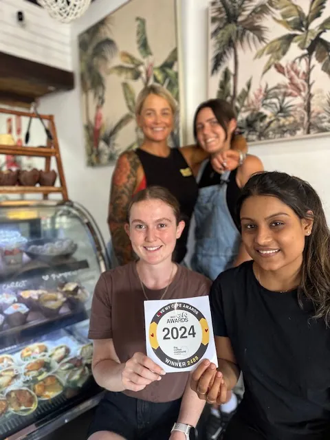 Two team members smiling beside the cake cabinet inside the cafe